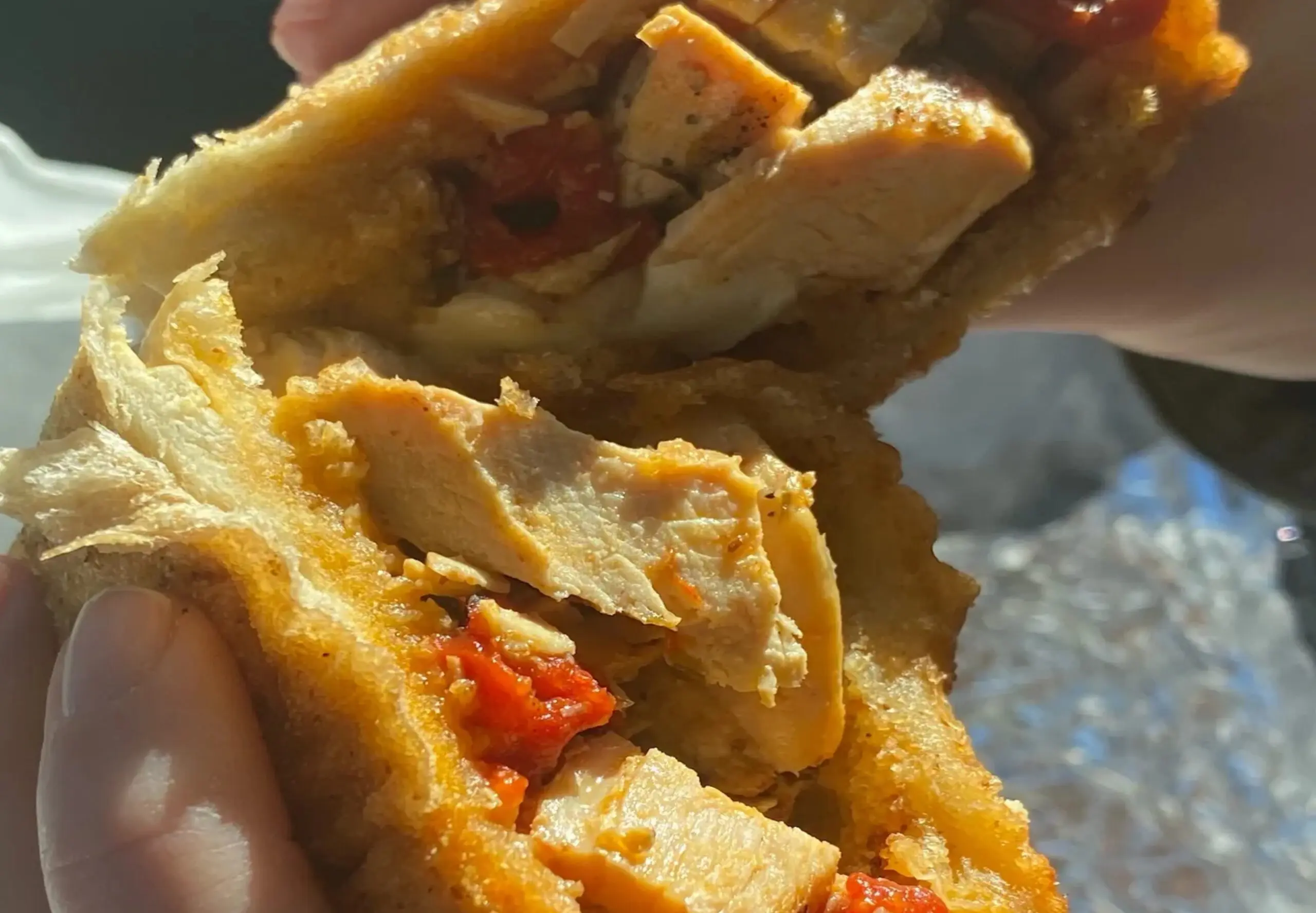 Chicken sandwich with red peppers being held.